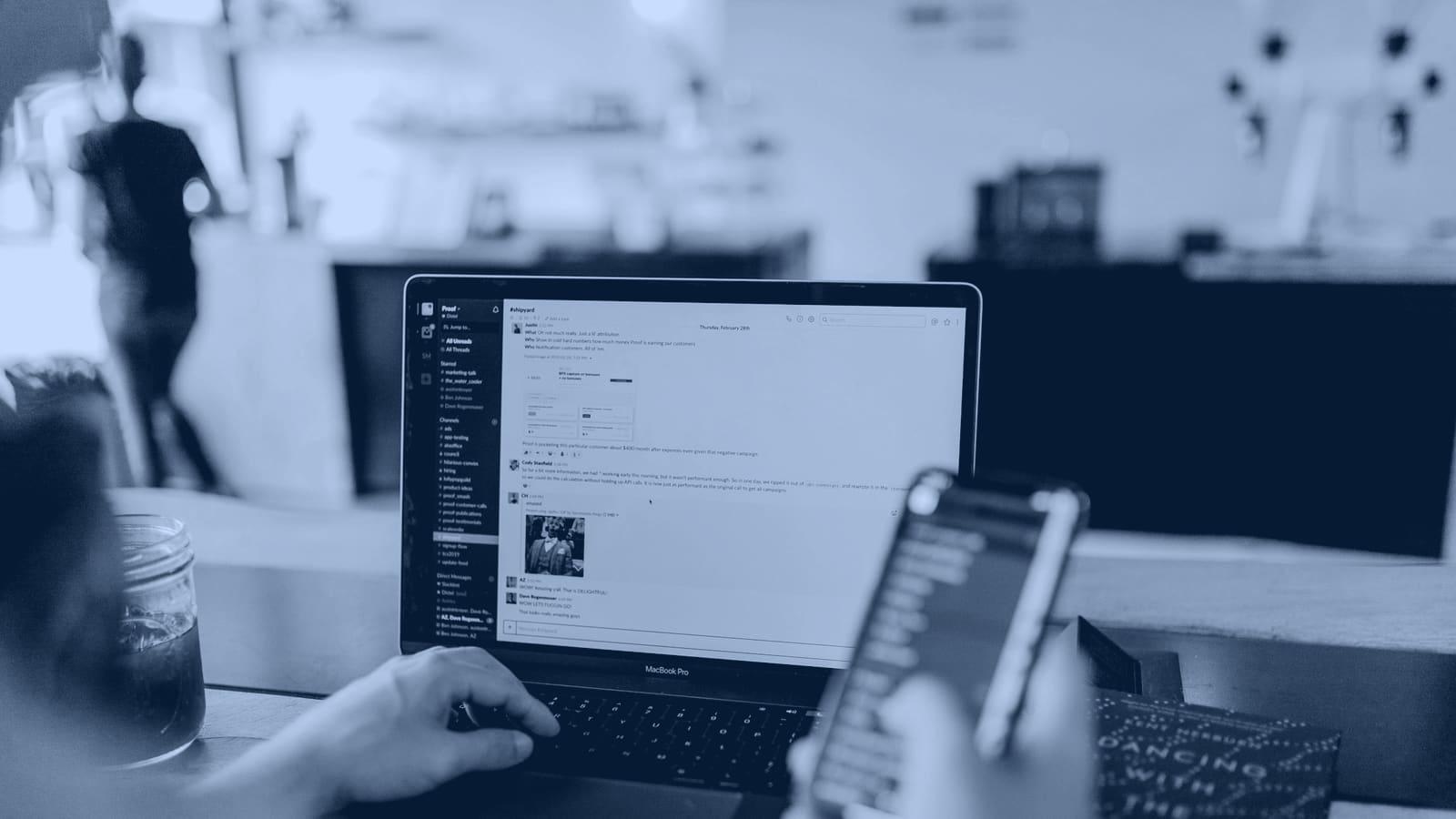 Someone reading messages on a laptop while holding a phone